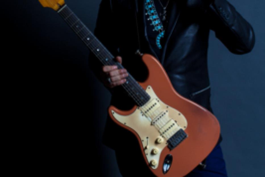 Ein Mann mit Sonnenbrille posiert mit einer orangefarbenen E-Gitarre.