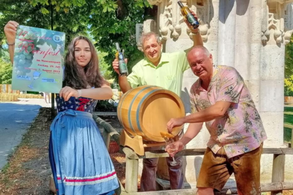 Drei Personen posieren mit einem Weinfass und einem Plakat für das Weinfest im Museumspark.