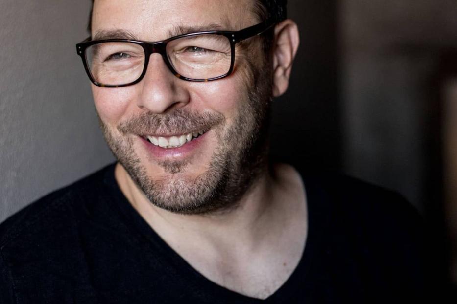 Ein lächelnder Mann mit Brille und Bartansatz.