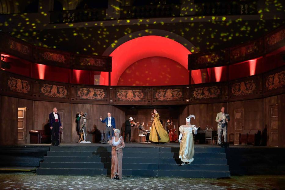 Eine Theaterszene mit mehreren Darstellern in historischen Kostümen auf einer Bühne.