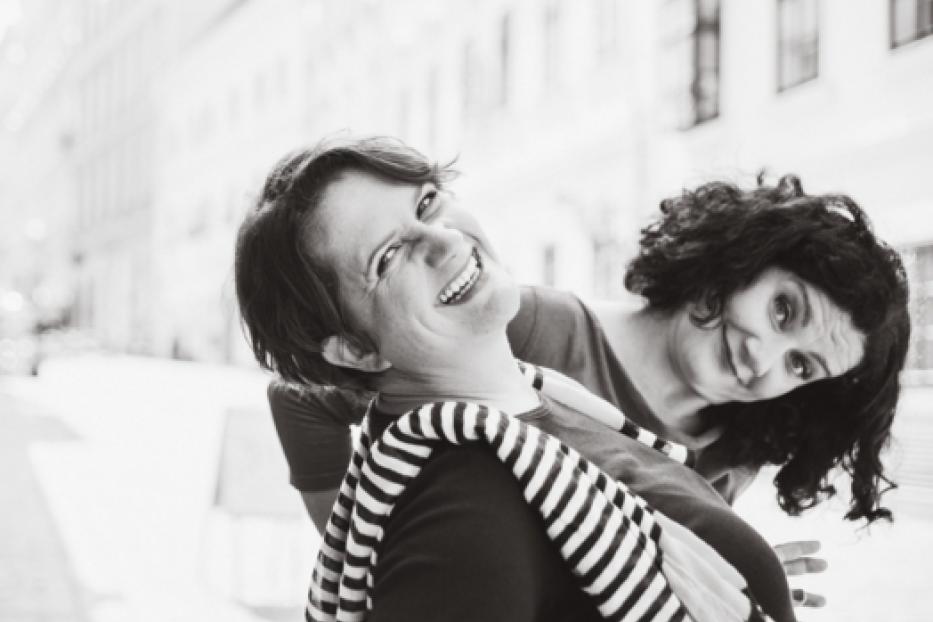 Zwei Frauen lachen und posieren auf der Straße für ein Schwarzweißfoto.