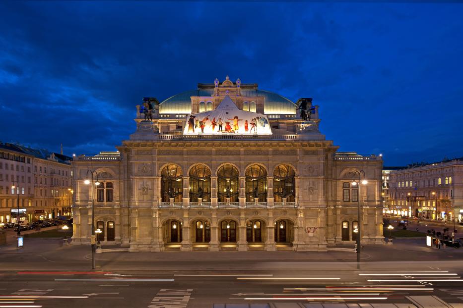 Die Wiener Staatsoper erstrahlt im Abendlicht unter einem tiefblauen Himmel.