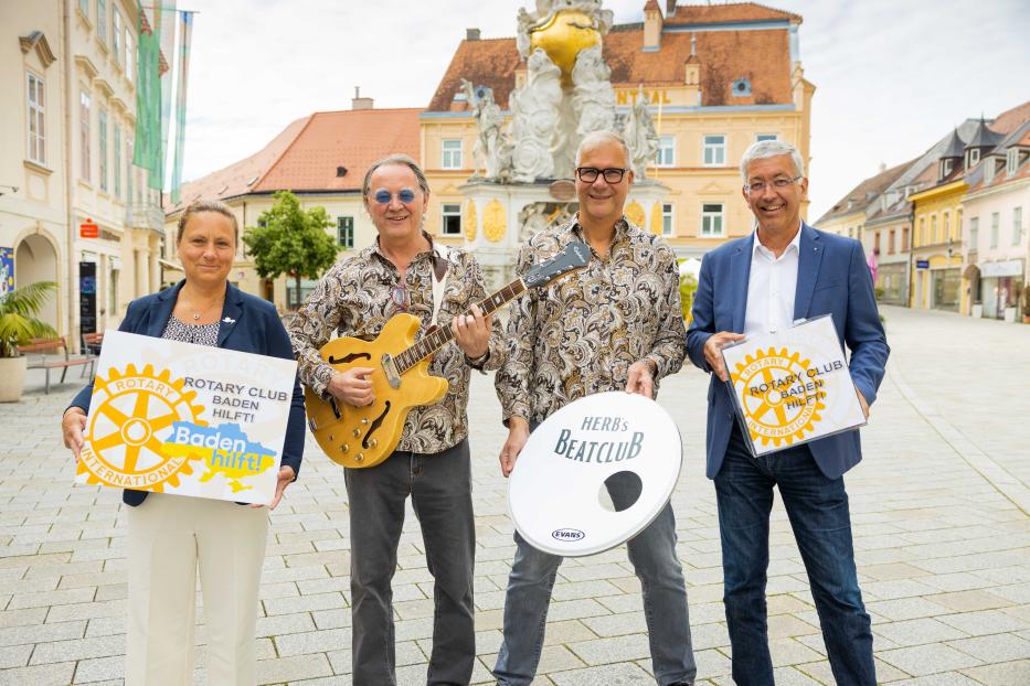 Vier Personen posieren mit Gitarre, Trommel und Schildern des Rotary Clubs Baden vor einem Gebäude.
