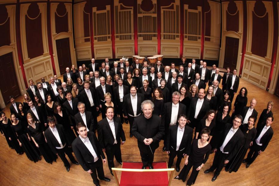 Ein großes Orchester und ein Chor stehen auf einer Bühne vor einem Konzert.