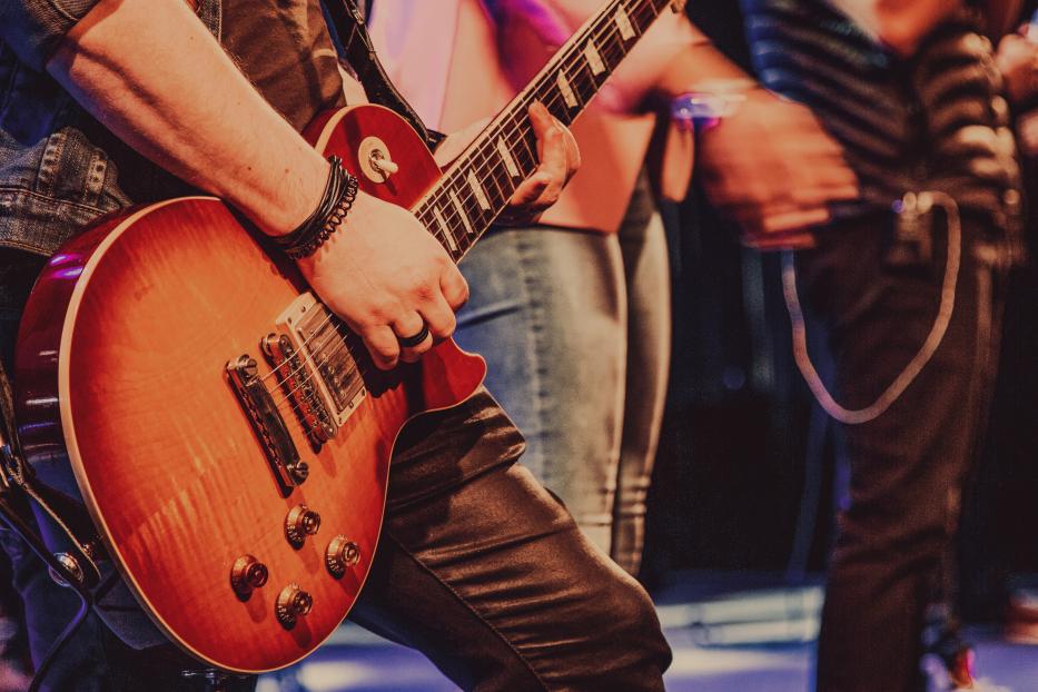Ein Gitarrist spielt auf einer rotbraunen E-Gitarre auf der Bühne.