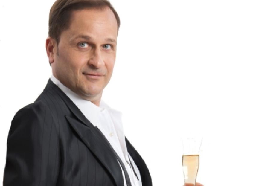 Ein Mann im Anzug hält ein Glas Sekt in der Hand.