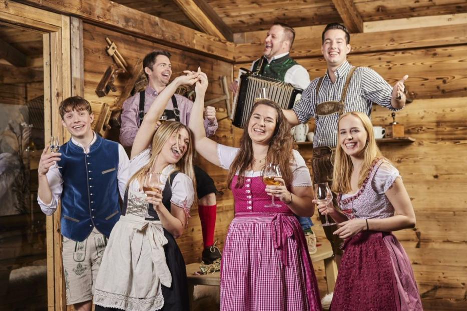 7 Personen in Tracht beim Lachen, Trinken und Musizieren.