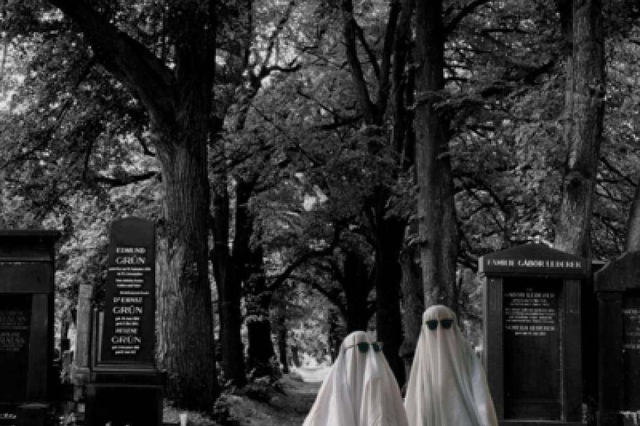 Zwei als Geister verkleidete Personen mit Sonnenbrillen stehen auf einem Friedhof.