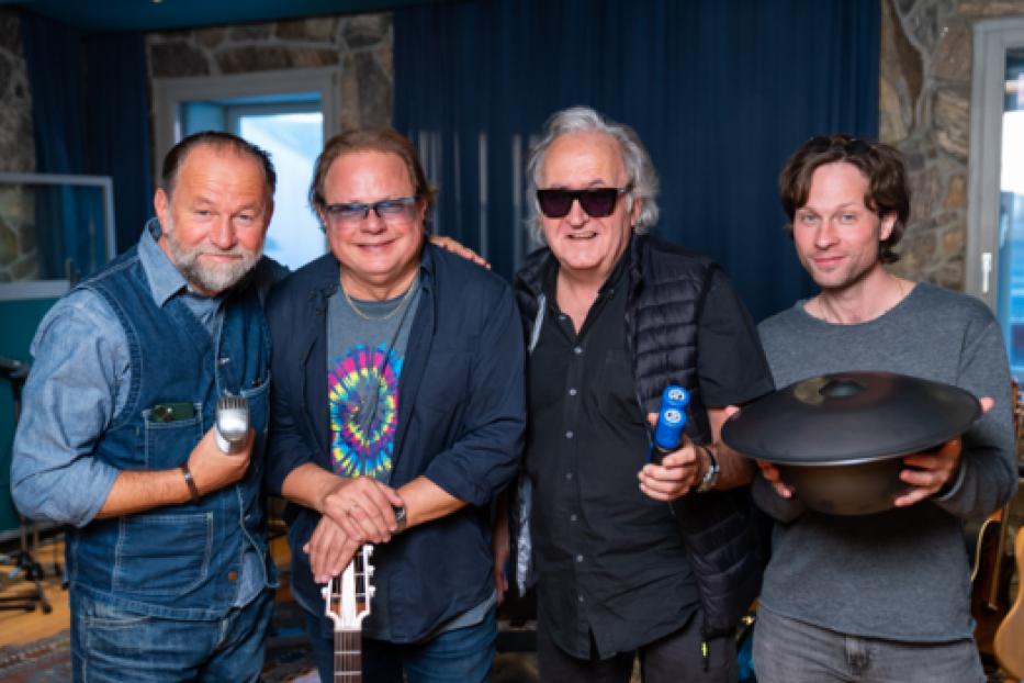 Vier Männer posieren in einem Musikstudio mit Instrumenten für ein Foto.