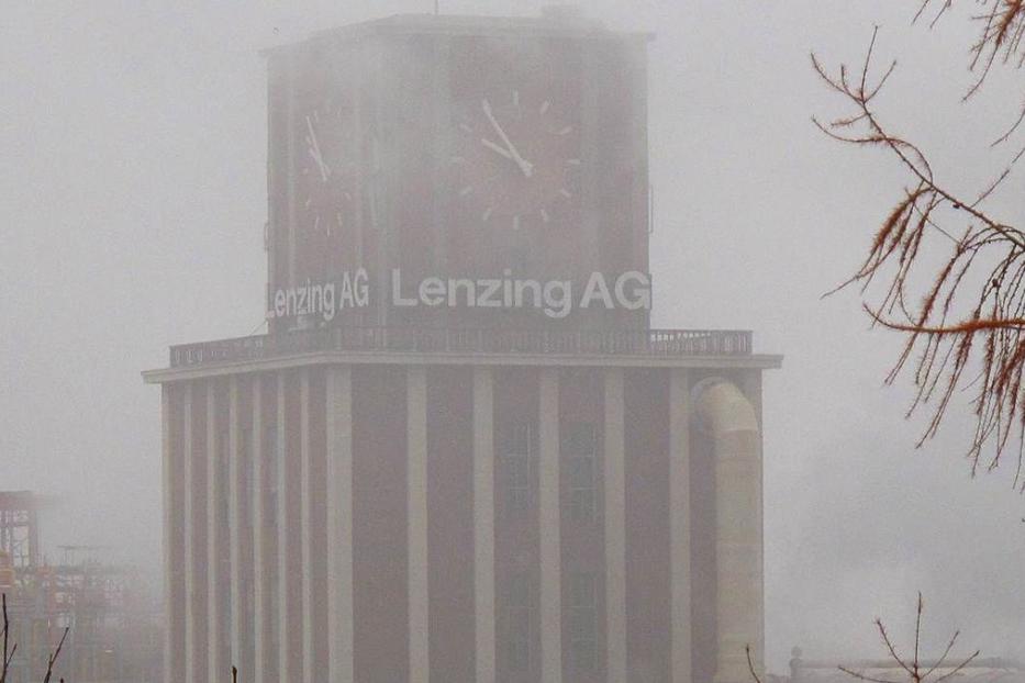 Ein hoher Turm mit der Aufschrift „Lenzing AG“ ist im Nebel zu sehen.