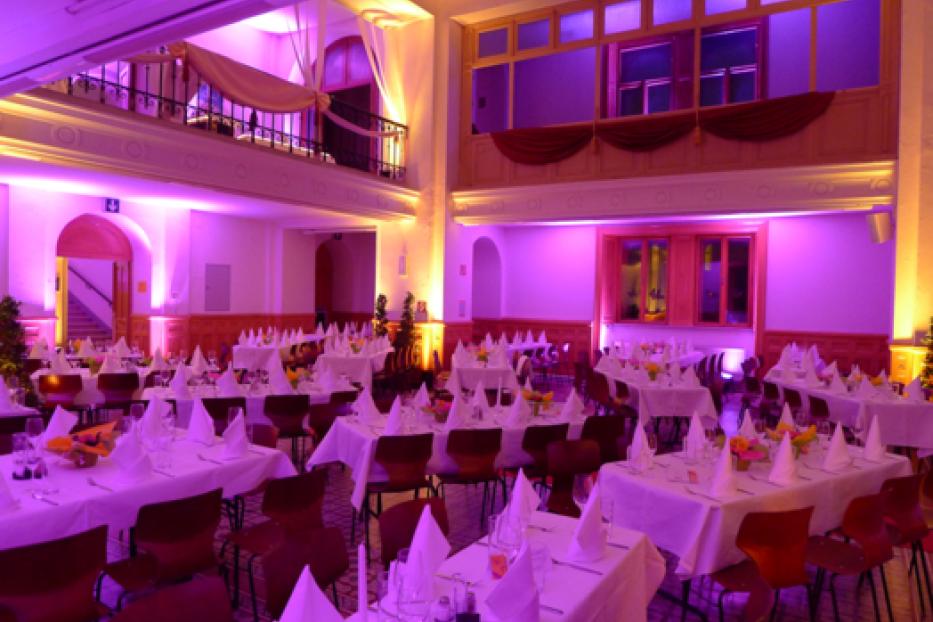 Ein festlich dekorierter Saal mit Tischen und Stühlen, beleuchtet in violettem Licht.