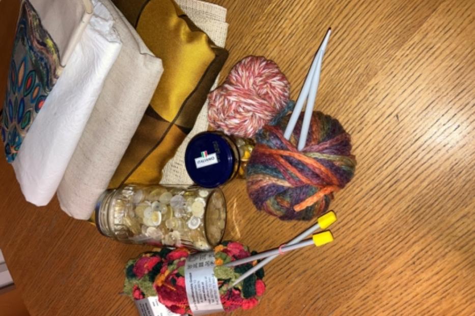 Verschiedene Wollknäuel, Stricknadeln und Stoffe liegen auf einem Tisch.