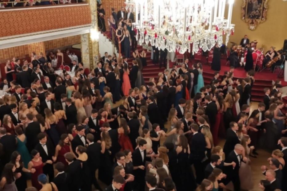 Ein großer Ballsaal mit vielen tanzenden Paaren unter einem Kronleuchter.