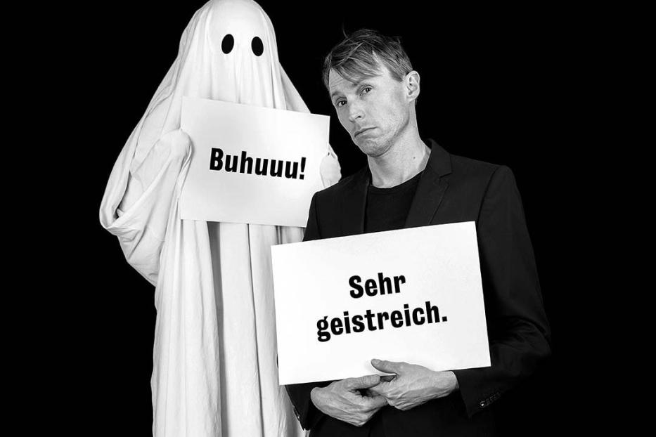 Ein Mann im Anzug posiert mit einem Geist, beide halten Schilder hoch.