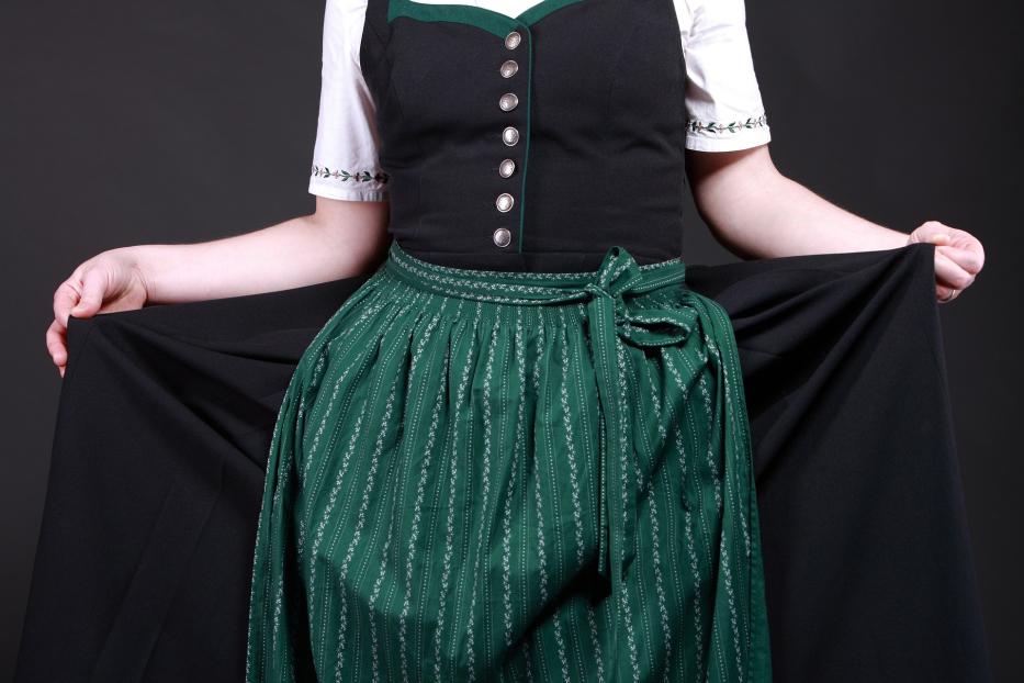 Eine Frau in einem Dirndl hält den Rockstoff zur Seite.