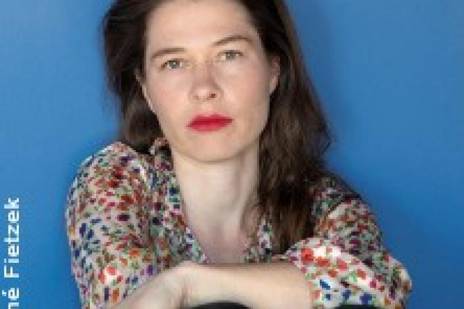Eine Frau mit roten Lippen sitzt vor einem blauen Hintergrund.