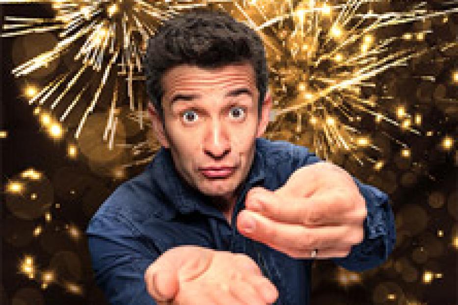 Ein Mann mit offen Händen steht vor einem Hintergrund aus goldenem Feuerwerk.