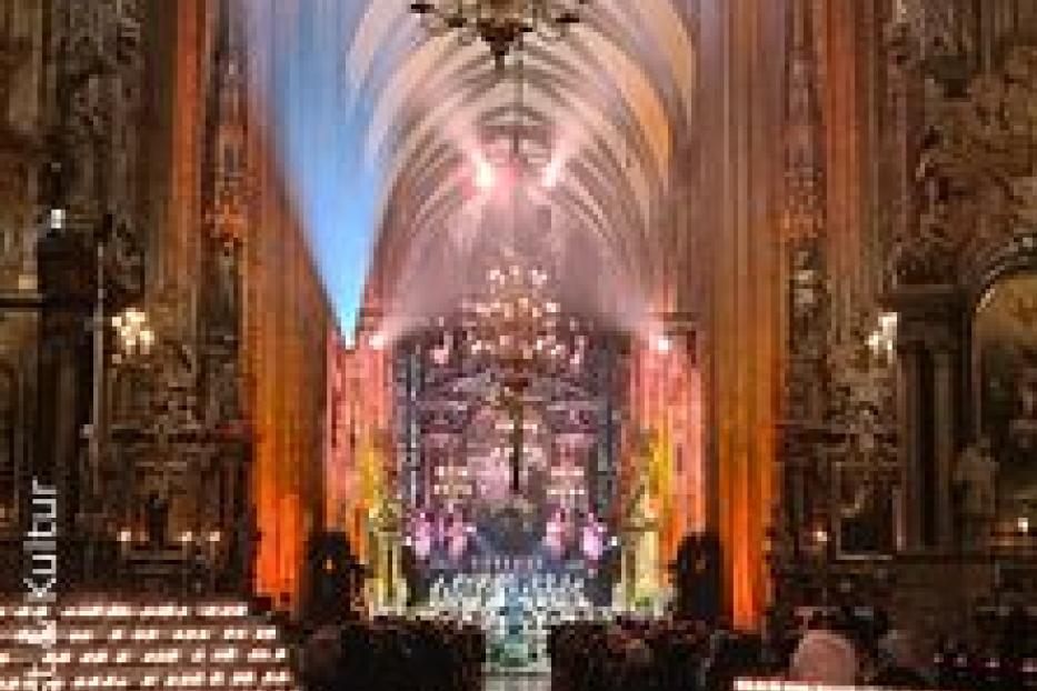 Innenansicht einer Kirche mit vielen Kerzen und einer Aufführung im Altarbereich.