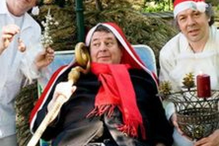 Drei Männer mit Weihnachtsmützen posieren für ein Foto, einer sitzt mit einem Stock in einem Stuhl.