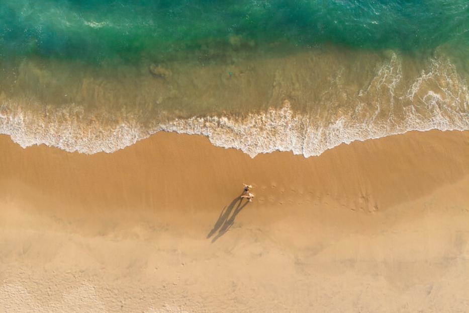 Eine Drohnenaufnahme von Menschen, die am Varkala Strand stehen. Die Wellen branden an.