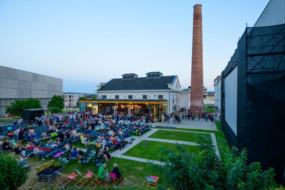 Ein Open-Air-Kino mit vielen Zuschauern vor einer großen Leinwand.