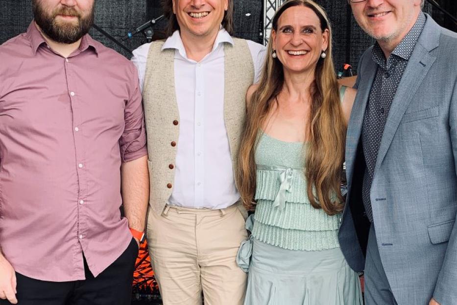 Vier Personen posieren vor einer Bühne für ein Gruppenfoto.