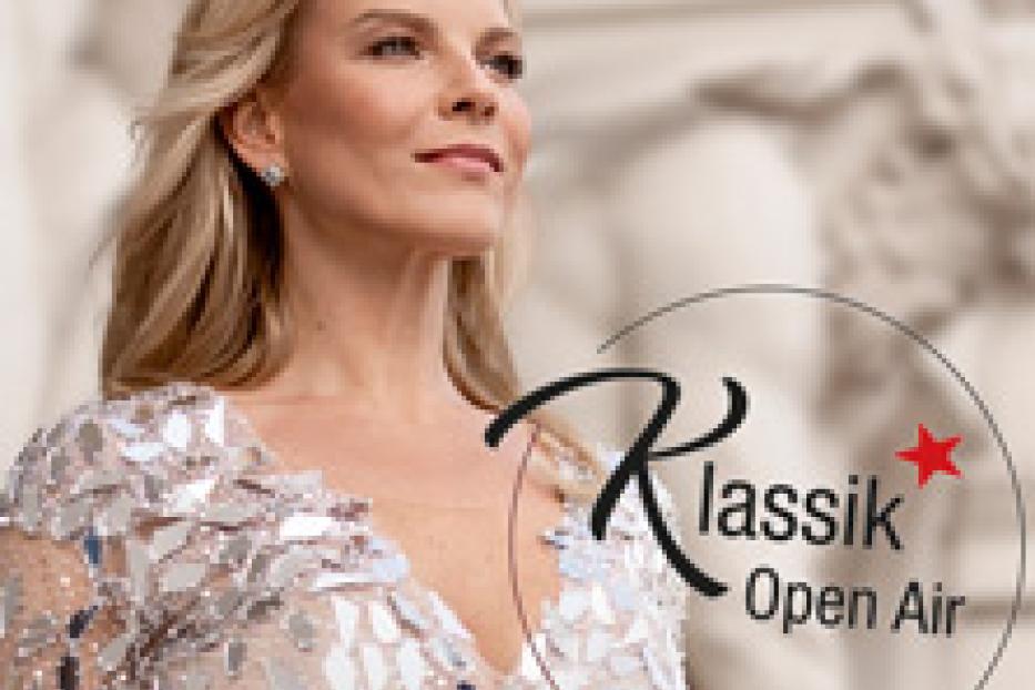 Eine blonde Frau im Abendkleid vor einem Gebäude mit der Aufschrift „Klassik Open Air“.