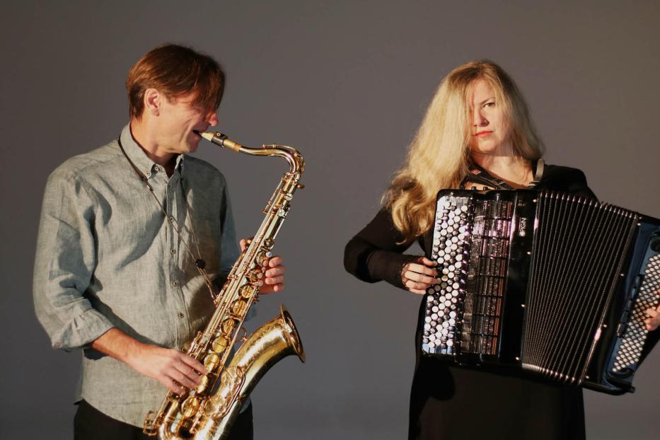 Ein Mann spielt Saxophon, während eine Frau Akkordeon spielt.