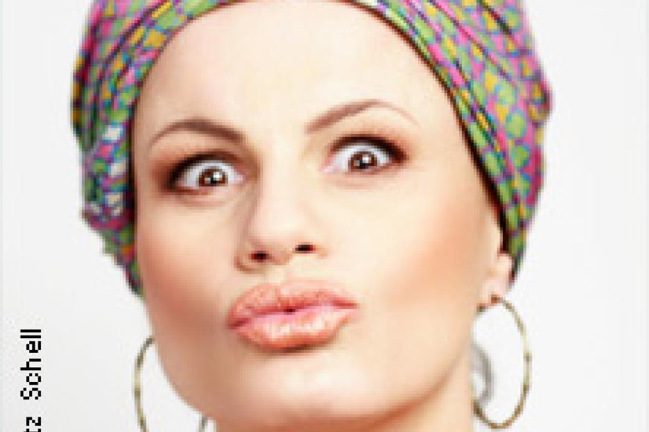 Eine Frau mit Turban und großen Ohrringen schaut überrascht in die Kamera.