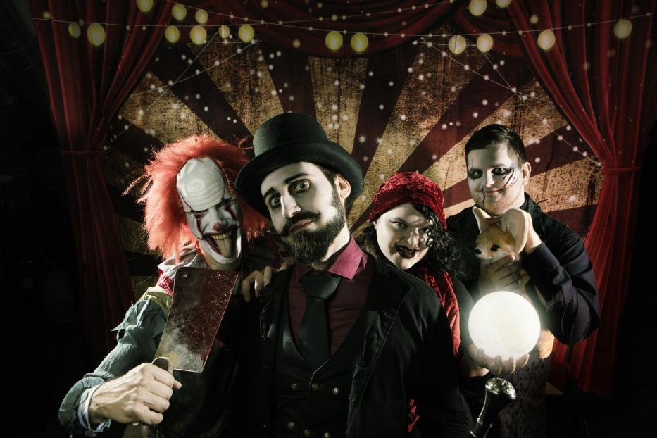 Ein Horrorclown mit Beil, ein Zirkusdirektor, eine Wahrsagerin und ein Raubtierdompteur posieren vor einem Zirkuszelt.