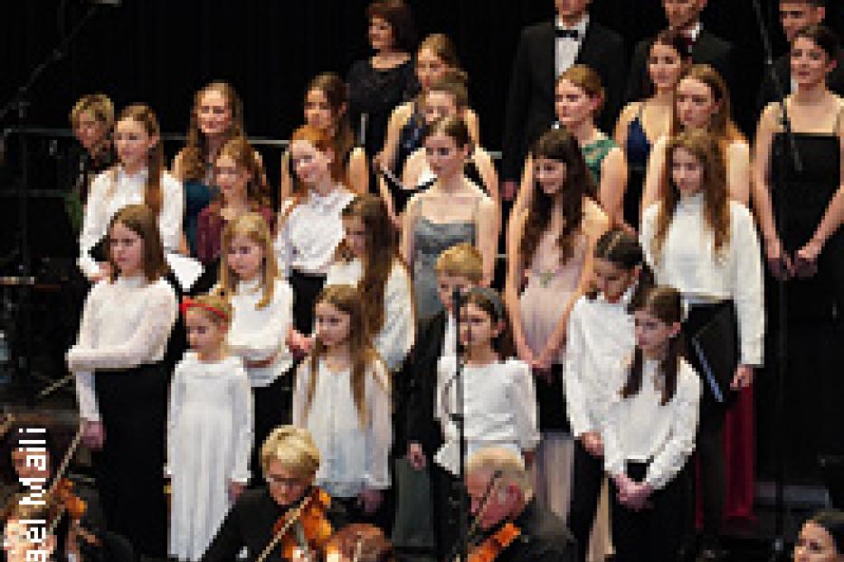 Ein Chor mit jungen Sängerinnen und Sängern steht vor einem Orchester.