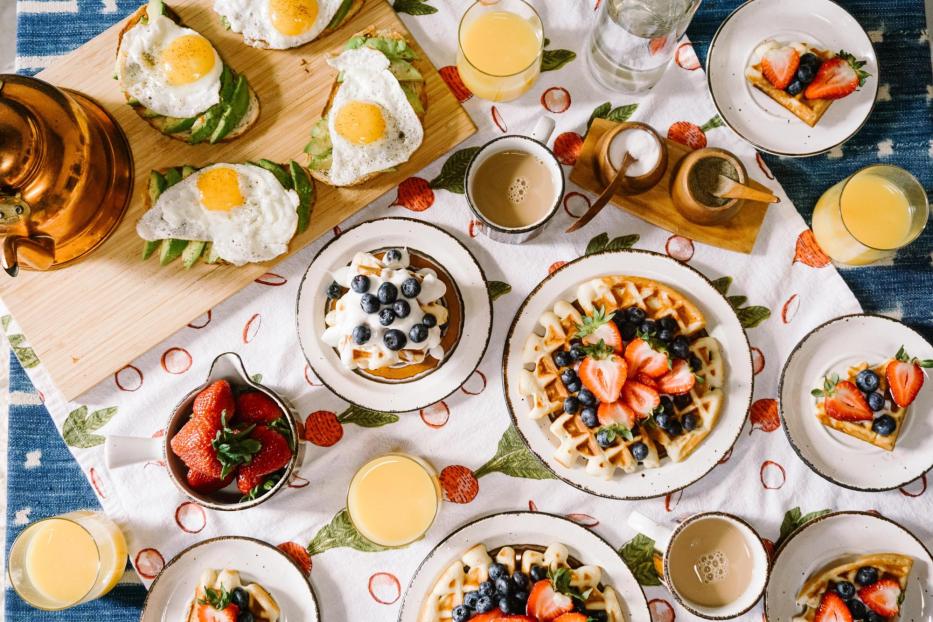 Ein reich gedeckter Frühstückstisch, mit Waffeln, Spiegelei auf Brot, Kaffees und Säften