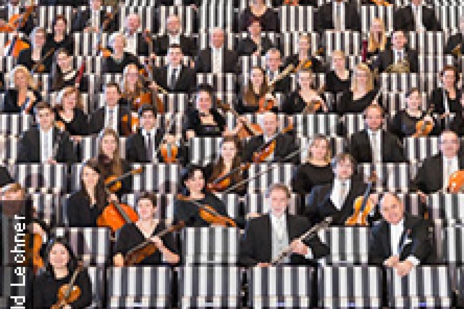 Ein Orchester sitzt auf einer gestreiften Tribüne und spielt.