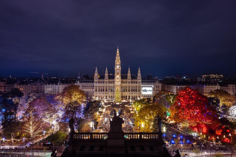 Blick auf das Rathaus vom Burgtheater aus gesehen. Mittig der Markt, links und rechts die beleuchtete Weihnachtswelt im Park.