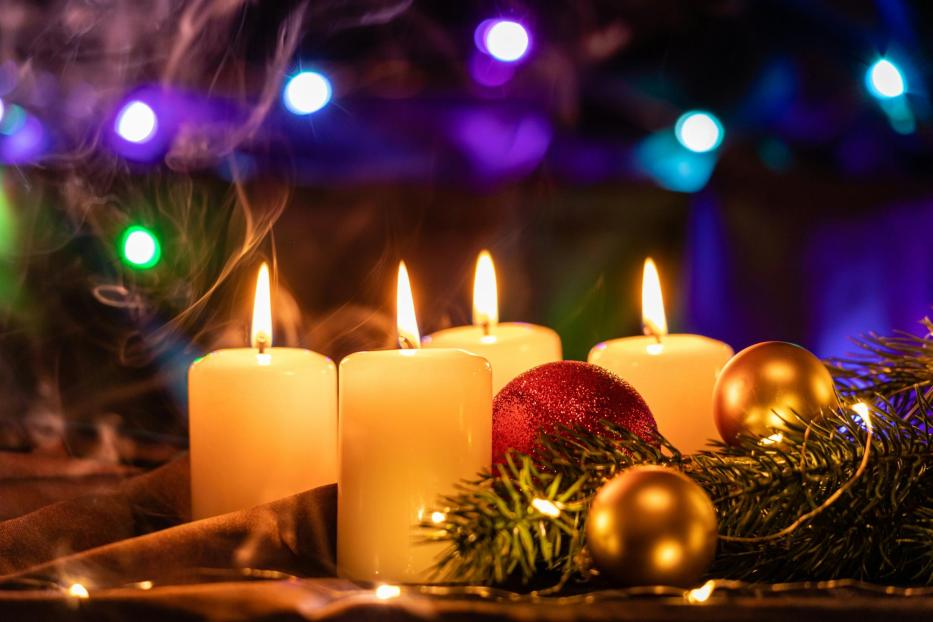 Vier brennende Kerzen stehen neben Weihnachtskugeln und Tannenzweigen.
