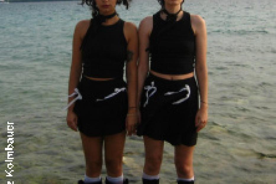 Zwei junge Frauen stehen im Wasser vor einer bewaldeten Insel.