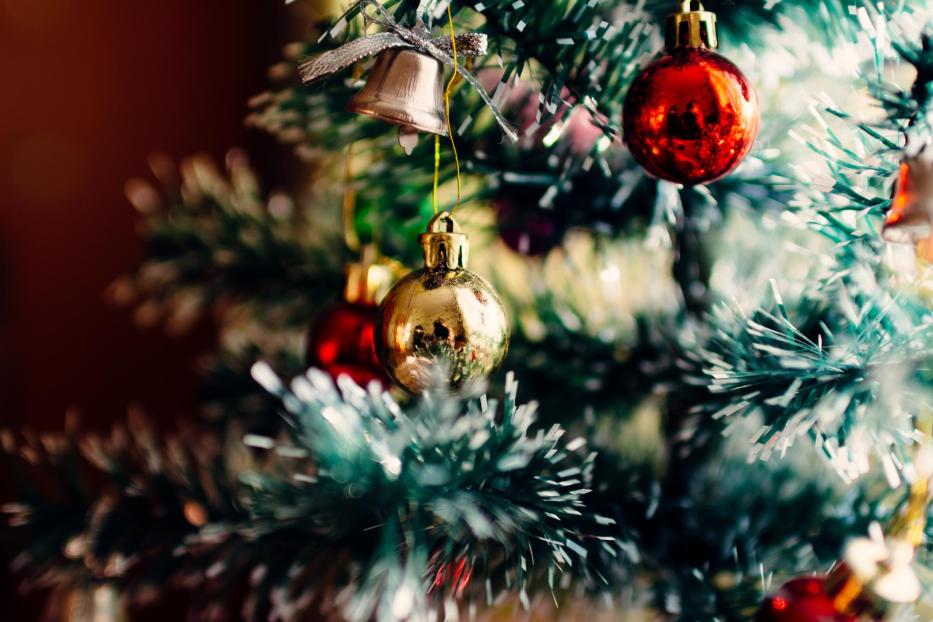 Ein Weihnachtsbaum ist mit roten und goldenen Kugeln sowie einer Glocke geschmückt.