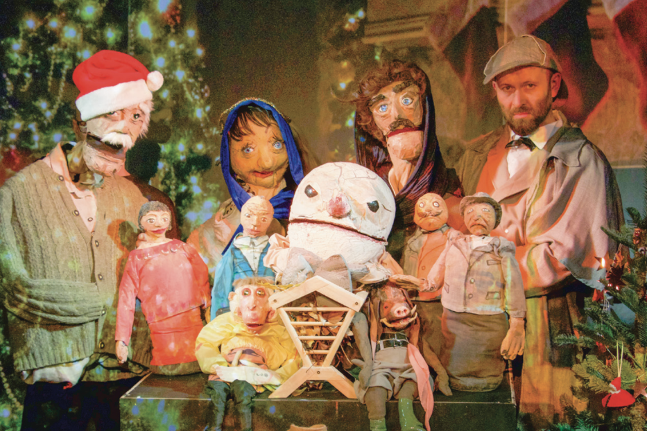 Eine Gruppe von Marionetten, darunter eine Weihnachtskrippe, vor einem Weihnachtsbaum.