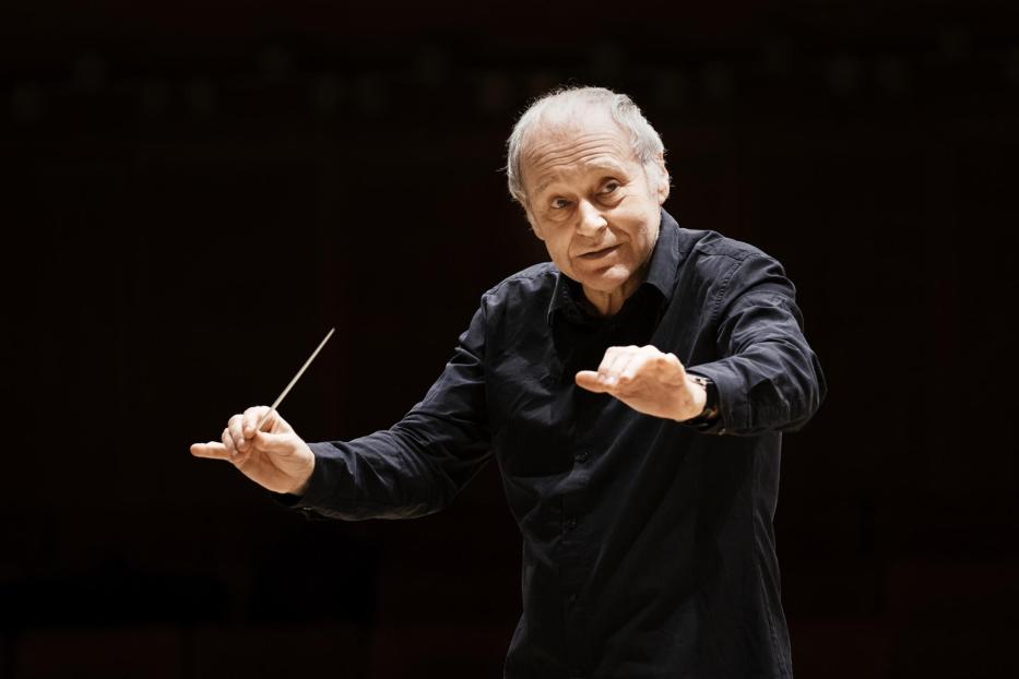 Ein älterer Mann mit einem Taktstock dirigiert ein Orchester.