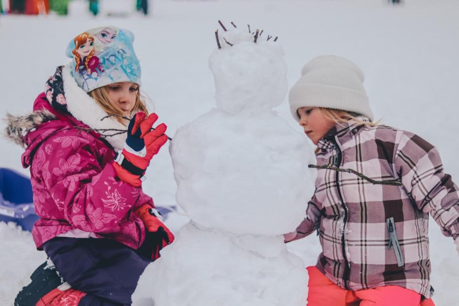 Zwei Kinder bauen einen Schneemann.