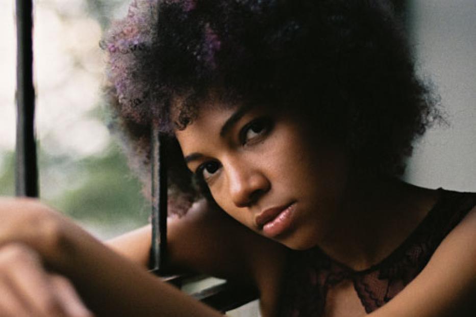 Eine junge Frau mit Afro-Haar lehnt am Fenster.