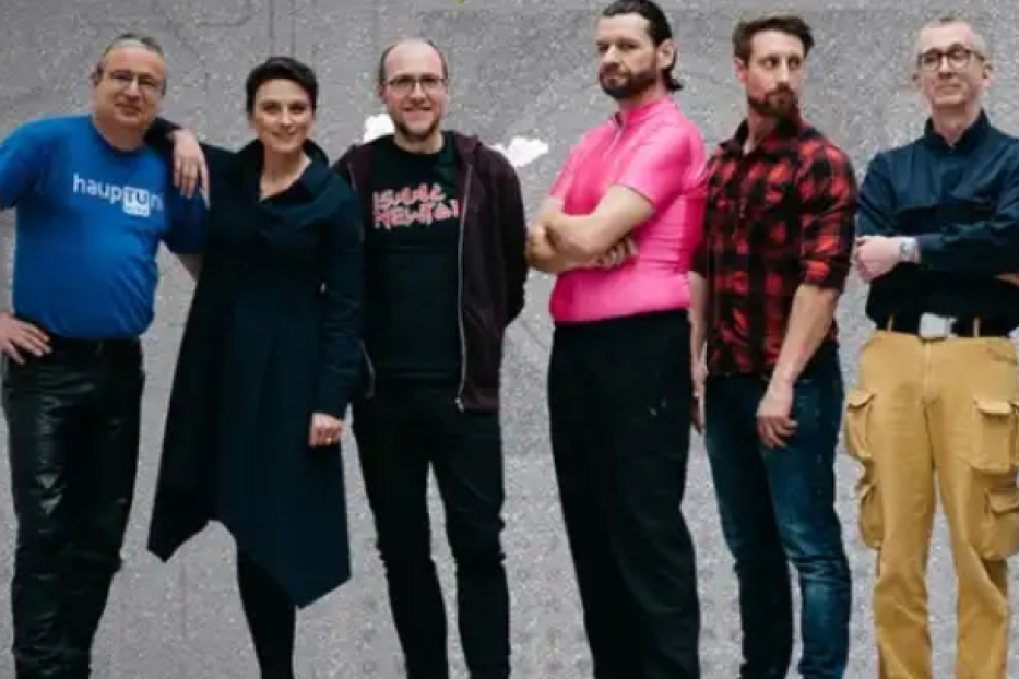 Eine Gruppe von sechs Personen posiert vor einer grauen Wand.