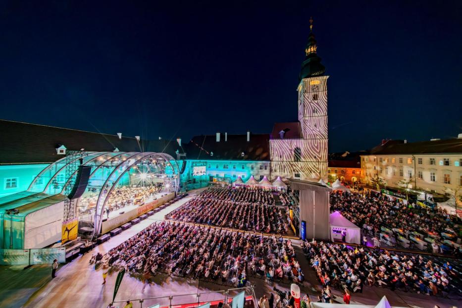 Eine Open-Air-Veranstaltung mit Publikum vor einer beleuchteten Kirche.