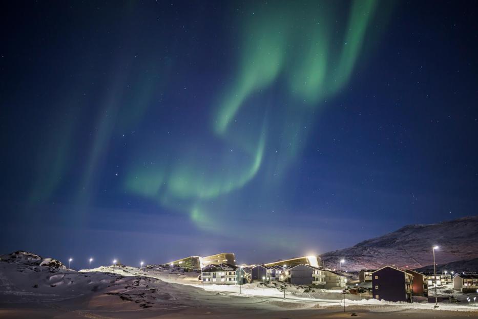 Über einer verschneiten Siedlung tanzen grüne Nordlichter am Nachthimmel.