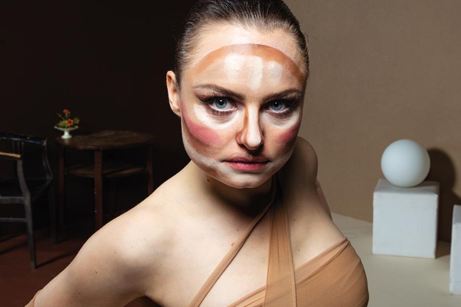 Eine Frau mit Make-up-Konturierung im Gesicht posiert selbstbewusst.