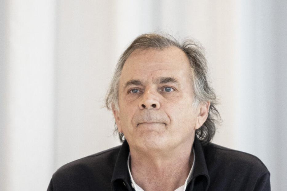 Markus Hinterhäuser sitzt an einem Tisch mit Wasserflasche und Glas.