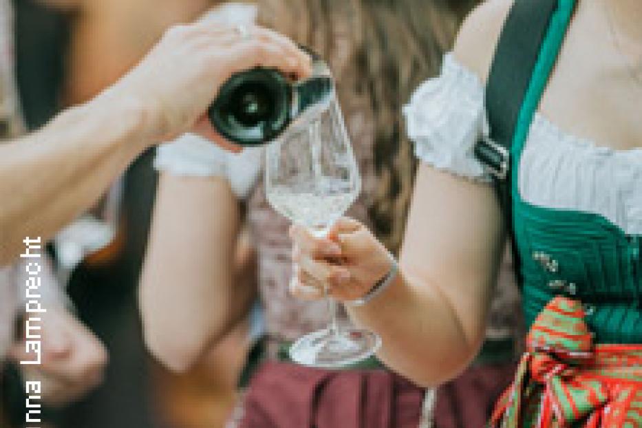 Eine Frau im Dirndl gießt Weißwein in ein Glas.
