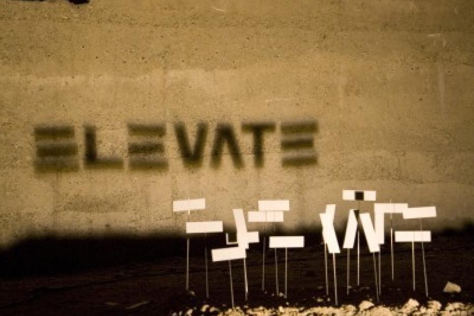 Auf einer Betonwand steht das Wort „Elevate“ und davor stehen kleine Schilder.
