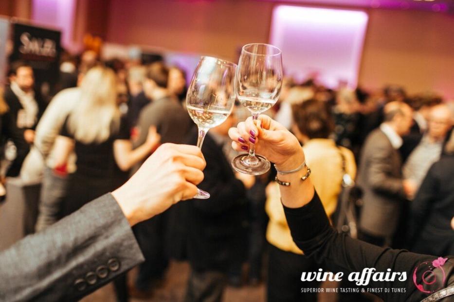 Zwei Personen stoßen auf einer Weinprobe mit ihren Weingläsern an.