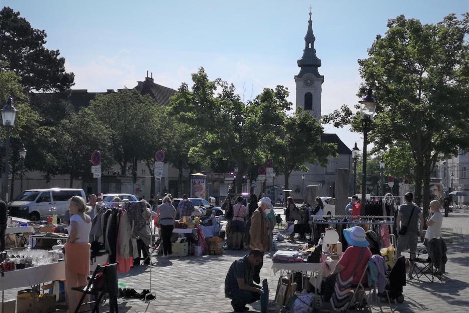 Ein belebter Flohmarkt findet auf einem Platz mit einer Kirche im Hintergrund statt.